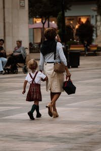 A mother and daughter walk hand in hand through a city street, showcasing urban family life.