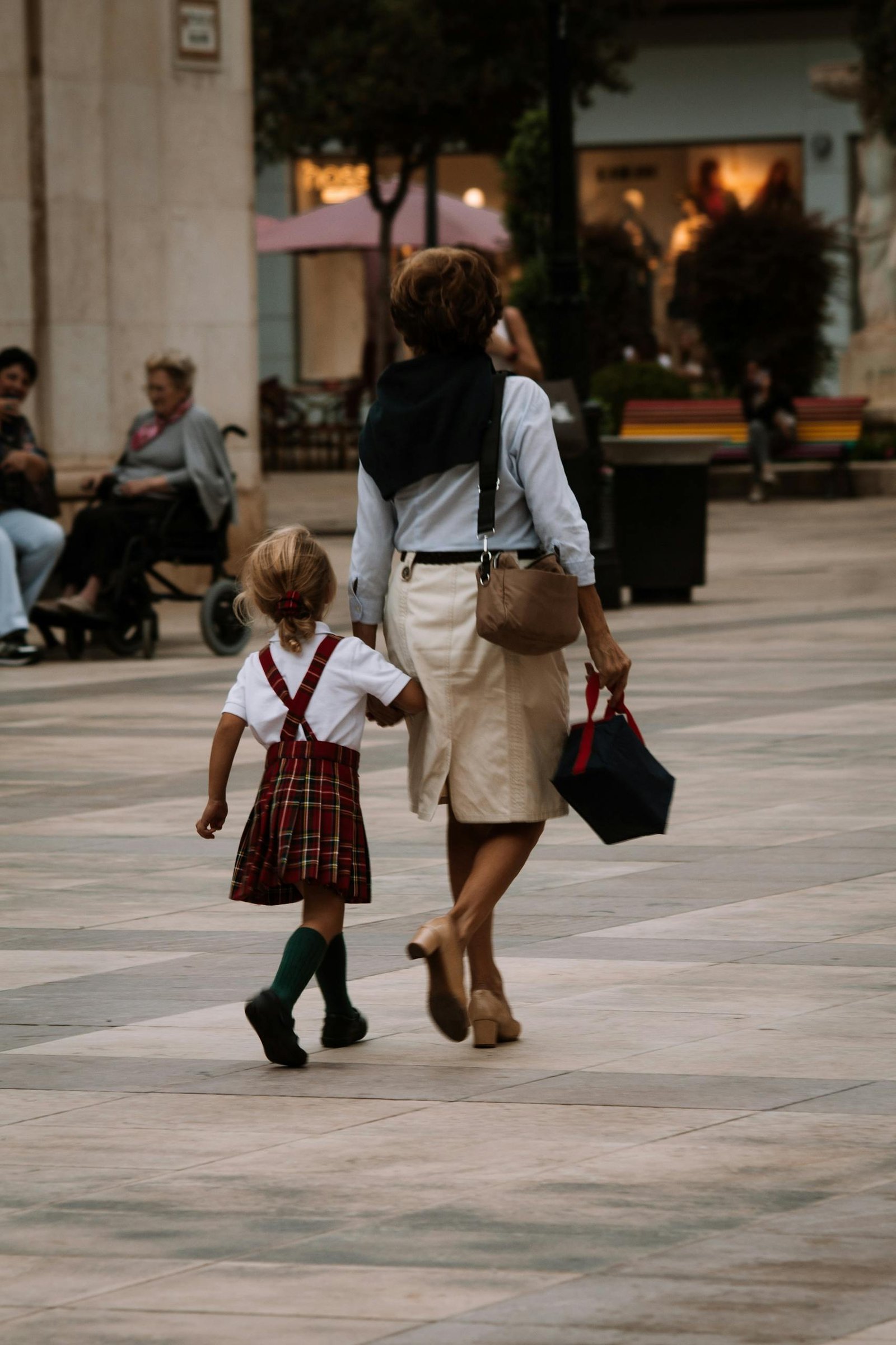 A mother and daughter walk hand in hand through a city street, showcasing urban family life.