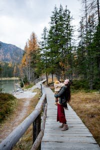 A joyful mother and child enjoying a scenic nature walk on a wooden path surrounded by trees.